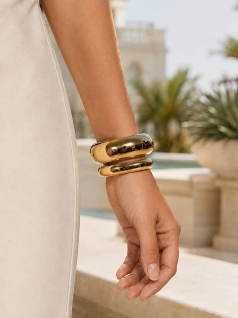 Wide and slim gold bangles stacked together on the wrist with a white dress