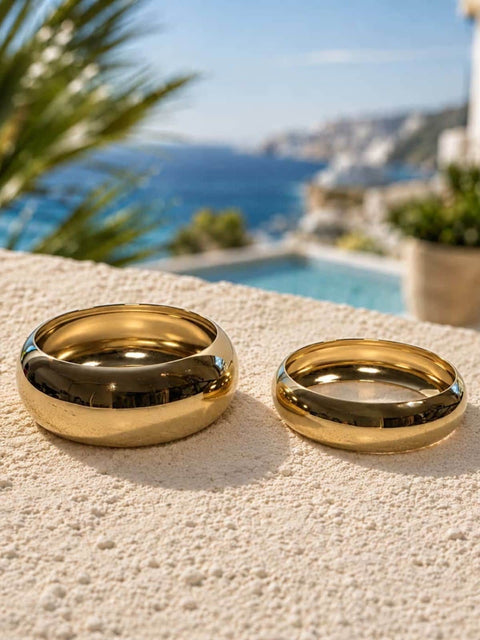 Two piece polished gold bangle set displayed on a textured stone surface