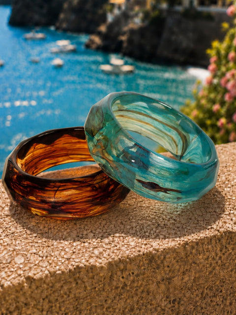 Two thick, faceted mavi bangles One bangle is a translucent teal blue and green marbled swirls, and the other is a dark amber-brown with darker brown swirls.