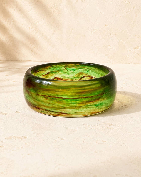 A thick, wide bangle bracelet made of marbled green acrylic with brown and  swirls