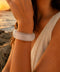 Zeni wide acrylic bangle in white marble displayed on natural coastal rocks at sunset