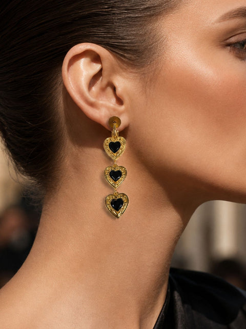 Gold drop earring with three stacked heart-shaped each heart featuring a black center stone.