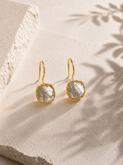 Front view of gold hook earrings with clear faceted stones featuring gold specks.