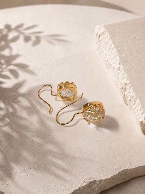 Back view of gold hook earrings with ornate gold settings and clear stones containing gold specks