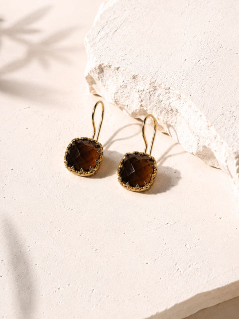 A pair of gold-tone drop earrings with a square, bezel-set brown gemstones. 
