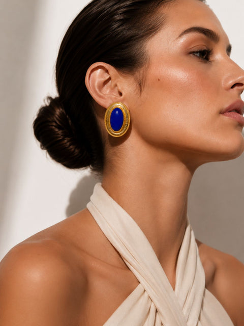 Close up of rhodes gold oval earrings with deep blue stones and textured gold finish