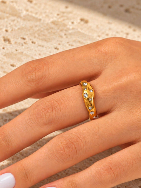 Gold statement ring featuring an irregular curved design with sparkling clear stones in different sizes